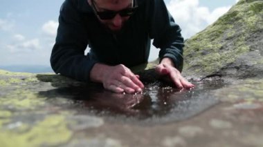 Susamış ve zinde bir turist sert dağ koşullarında küçük bir su birikintisinden su içiyor. Dağ yaşamı konsepti. Kayalık dağlarda zor şartlarda bir turist.