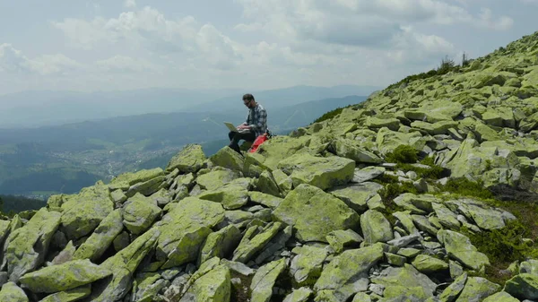 男はラップトップで働き 岩山の頂上に座っている 山での休暇中にリモート作業 世界中のリモートワークのコンセプト — ストック写真