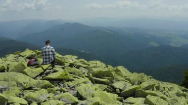 Bir adam kayalık bir dağın tepesinde otururken dizüstü bilgisayarda çalışıyor. Dağlarda tatildeyken uzaktan kumandalı iş. Dünyanın herhangi bir yerinde uzaktan çalışma kavramı.