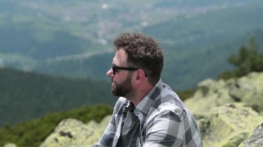 Bir adam kayalık bir yamaçta otururken şişeden su içer. Yürüyüş sırasında bir adam şişeden su içer. Dağlarda tek bir yürüyüş.