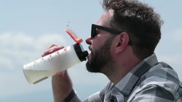 Homem Bebe Água Uma Garrafa Enquanto Está Sentado Uma Encosta — Vídeo de Stock