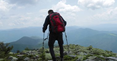 Dağlara bir gezi, bir turist sırt çantası ve çubuklarla gider, yüksek dağların kayalık arazisinde seyahat eder, bağımsız, kayalıklarda yalnız gezer..