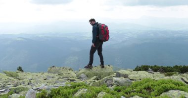 Orta yaşlı bir sırt çantalı adam inanılmaz bir manzarayla yavaşça dağın kenarına yaklaşıyor. Yüksek dağlarda tek başına yürüyüş kavramı..
