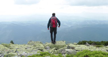 Orta yaşlı bir sırt çantalı adam inanılmaz bir manzarayla yavaşça dağın kenarına yaklaşıyor. Yüksek dağlarda tek başına yürüyüş kavramı..