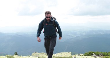 Orta yaşlı bir sırt çantalı adam inanılmaz bir manzarayla yavaşça dağın kenarına yaklaşıyor. Yüksek dağlarda tek başına yürüyüş kavramı..