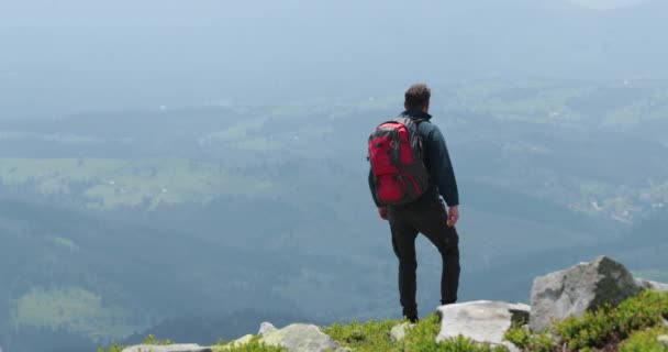 中年のバックパッカーの男性は 信じられないほどの景色でゆっくりと山の端に近づきます 高山でのソロハイキングのコンセプト — ストック動画