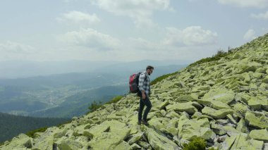 Dev taşlarla kaplı bir dağ yamacı boyunca yürüyen bir adam. Solo turizm. Zor yürüyüş, macera turizmi konsepti.