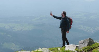 Dağın tepesindeki bir gezgin telefonla konuşuyor, fotoğraf çekiyor ve görüntülü konuşma yapıyor. Dünyanın uzak yerlerinde iletişim kavramı.