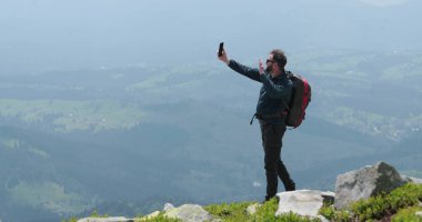 Dağın tepesindeki bir gezgin telefonla konuşuyor, fotoğraf çekiyor ve görüntülü konuşma yapıyor. Dünyanın uzak yerlerinde iletişim kavramı.