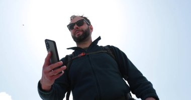 Bir adam yürürken sırt çantasıyla duran biriyle telefonda konuşuyor. İletişim, turizm, yürüyüş konsepti