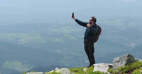 Dağın tepesindeki bir gezgin telefonla konuşuyor, fotoğraf çekiyor ve görüntülü konuşma yapıyor. Dünyanın uzak yerlerinde iletişim kavramı.