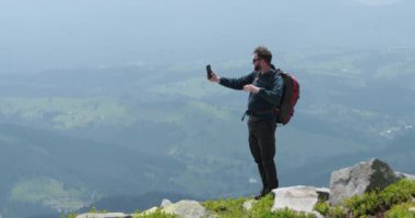 Dağın tepesindeki bir gezgin telefonla konuşuyor, fotoğraf çekiyor ve görüntülü konuşma yapıyor. Dünyanın uzak yerlerinde iletişim kavramı.