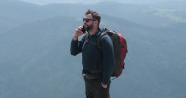 Dağın tepesindeki bir gezgin telefonla konuşuyor, fotoğraf çekiyor ve görüntülü konuşma yapıyor. Dünyanın uzak yerlerinde iletişim kavramı.