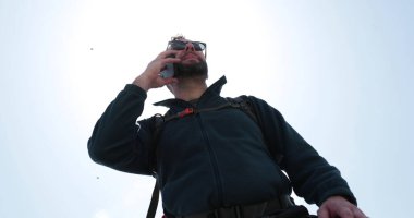 Bir adam yürürken sırt çantasıyla duran biriyle telefonda konuşuyor. İletişim, turizm, yürüyüş konsepti