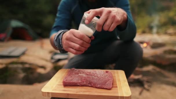 单一的游客烹调牛肉牛排 在大自然的背景上撒盐 慢动作 烹调烤肉用的肉制品 — 图库视频影像