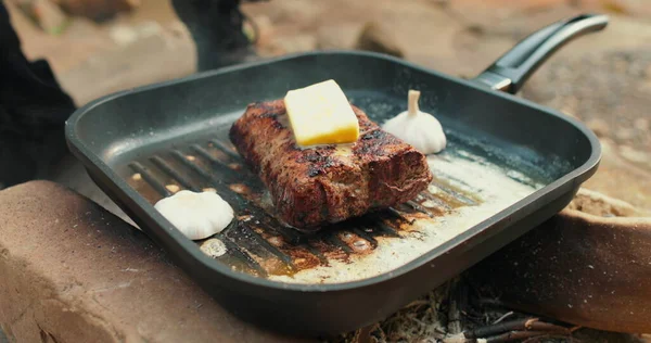 Adding butter to a steak on a hot pan in the process of grilling meat outdoors. Cooking meat on an open fire in nature on a tourist trip.
