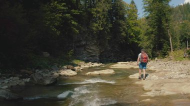 Dağ kanyonunda nehir boyunca yürüyen bir adamın hava görüntüsü. Dağ nehri boyunca tek bir turist yürüyüşü