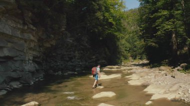 Dağ kanyonunda nehir boyunca yürüyen bir adamın hava görüntüsü. Dağ nehri boyunca tek bir turist yürüyüşü