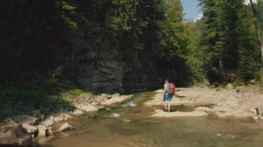 Dağ kanyonunda nehir boyunca yürüyen bir adamın hava görüntüsü. Dağ nehri boyunca tek bir turist yürüyüşü