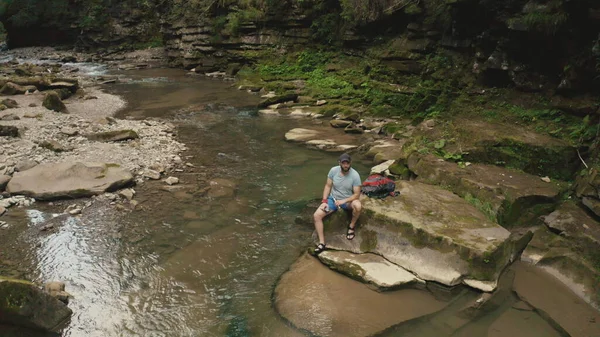 Yalnız bir gezgin nehir kıyısındaki bir taşın üzerinde dinleniyor. Bir İHA 4K görüntüsü.