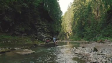 Yalnız bir gezgin nehir kıyısındaki bir taşın üzerinde dinleniyor. Bir İHA 4K görüntüsü.