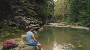 Yalnız bir gezgin nehir kıyısındaki bir taşın üzerinde dinleniyor. Bir İHA 4K görüntüsü.