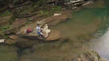 Yalnız bir gezgin nehir kıyısındaki bir taşın üzerinde dinleniyor. Bir İHA 4K görüntüsü.