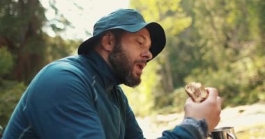 Bir erkek gezgin ormanda kamp kurdu ve çadırın önünde otururken yemek yiyor. Seyahat, yürüyüş ve kamp kavramı. Ormanda kamp yapan mutlu adam..