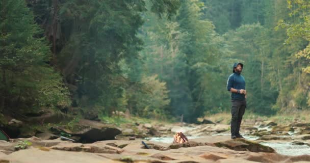 キャンプファイヤーの近くの森にいる男は 観光旅行中に休む 森でハイキングしたり 単一の旅行者の山でハイキング 観光キャンプの観光客 — ストック動画