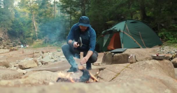 在森林篝火边 一名男性游客用一把小斧头砍柴 旅行者在准备生火的木柴 人在野外 野外远足者 野外生存 — 图库视频影像