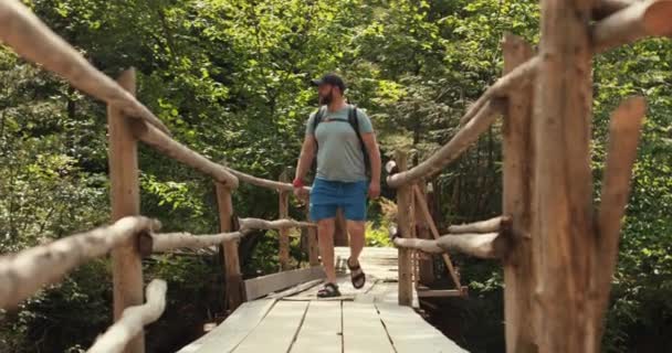 배낭을 하이킹 장비를 착용한 남자는 국립공원에서 서스펜션 다리를 건너다니며 산책합니다 — 비디오