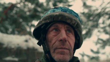 Close-up of an elderly Ukrainian soldier in military uniform and helmet. A Ukrainian soldier in a snowy trench.
