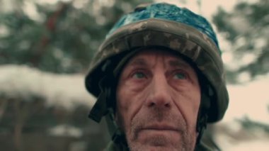 Close-up of an elderly Ukrainian soldier in military uniform and helmet. A Ukrainian soldier in a snowy trench.