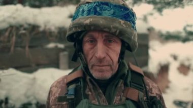 Close-up of an elderly Ukrainian soldier in military uniform and helmet. A Ukrainian soldier in a snowy trench.