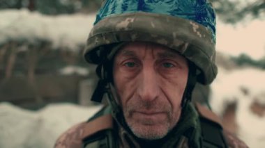 Close-up of an elderly Ukrainian soldier in military uniform and helmet. A Ukrainian soldier in a snowy trench.