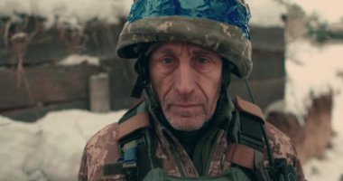 Close-up of an elderly Ukrainian soldier in military uniform and helmet. A Ukrainian soldier in a snowy trench.