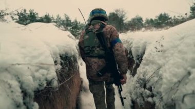 A soldier with a machine gun walks along the trench. A soldier in full armor walks along a trench. A soldier in the field. soldier with weapon in war.