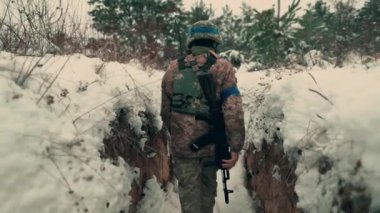 A soldier with a machine gun walks along the trench. A soldier in full armor walks along a trench. A soldier in the field. soldier with weapon in war.
