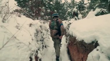 A soldier with a machine gun walks along the trench. A soldier in full armor walks along a trench. A soldier in the field. soldier with weapon in war.