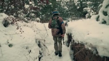 A soldier with a machine gun walks along the trench. A soldier in full armor walks along a trench. A soldier in the field. soldier with weapon in war.