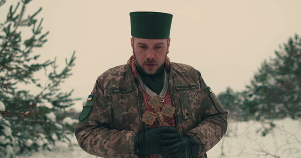 Chaplain in military uniform of the Ukrainian army. Portrait of a young chaplain in a snowy open space. Ukraine's war with Russia.