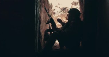 Yaşlı bir asker elinde makineli tüfekle hendekte oturur ve tüttürür. 2023 Ukrayna 'nın doğusunda askeri harekat. Ukrayna-Rusya savaşı.