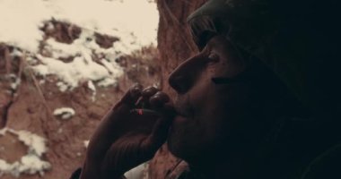Yaşlı bir asker elinde makineli tüfekle hendekte oturur ve tüttürür. 2023 Ukrayna 'nın doğusunda askeri harekat. Ukrayna-Rusya savaşı.