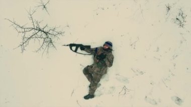 Ukrayna ordusunun yorgun ve bitkin bir askeri karlı zeminde makineli tüfekle yatıyor. İnsansız hava aracının görüntüleri tamamen dikey. Ukrayna Rusya Savaşı.