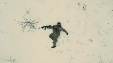 Ukrayna ordusunun yorgun ve bitkin bir askeri karlı zeminde makineli tüfekle yatıyor. İnsansız hava aracının görüntüleri tamamen dikey. Ukrayna Rusya Savaşı.