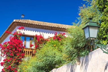 İspanya 'nın Granada kasabası. Parlak çiçekler beyaz bir binanın ön cephesinden aşağı akarak berrak mavi gökyüzüne karşı pitoresk bir manzara yaratır..