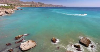 Nerja, Endülüs 'ün Costa del Sol sahil şeridi, Europa Meydanı' ndan manzaralı. Kıyı manzarası turkuaz su, yüzücüler, kayalar ve uzakta bir tekne..