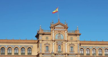 İspanya 'nın Endülüs şehrindeki Sevilla Meydanı' nda bulunan Espana Meydanı 'nda. Açık mavi gökyüzü altında İspanyol mimarisi. Karmaşık detayları ve gururla dalgalanan bir bayrağı olan güzel bir bina..
