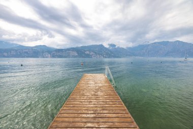 Pier leading into Lake Garda with mountains in background, view from Malcesine town on the eastern shore of the lake, Italy, Europe. clipart