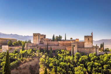 İspanya 'nın Granada kasabasındaki Mirador de San Nicolas' tan Alhambra Panoraması. Bereketli yeşil tepelere ve açık mavi gökyüzünün altındaki dağlara bakan antik kale..